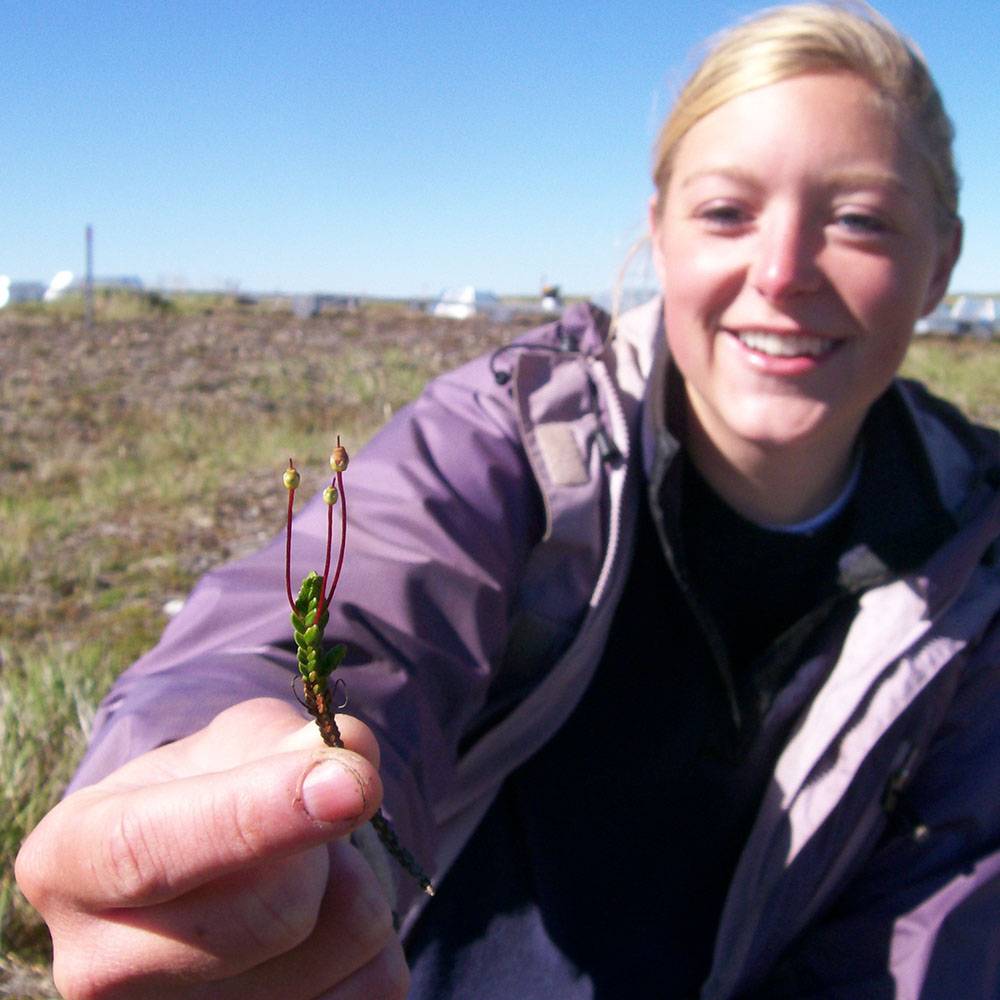 She smiles and holds up a plant to the camera.